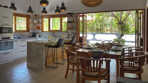 A modern kitchen with white cabinets, a central island, bar stools, and pendant lighting. - Lovina luxury pool villa at a magnificent location! (Lovina)