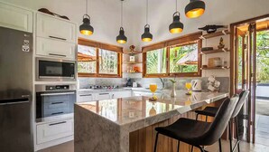 A modern kitchen with a central island, bar stools, and pendant lighting. - Lovina luxury pool villa at a magnificent location! (Lovina)