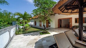 A patio with lounge chairs, a thatched roof structure, and a small garden area with a palm tree. - Lovina luxury pool villa at a magnificent location! (Lovina)