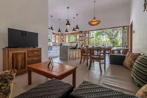Ein modernes Wohnzimmer mit Fernseher, Holzmöbeln und einem Essbereich mit Stühlen und einem Tisch.