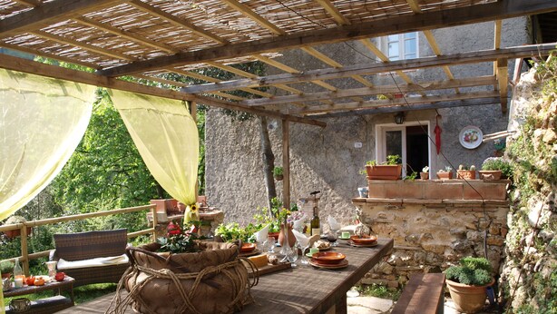 Un patio al aire libre con una mesa de madera, sillas y plantas en macetas.