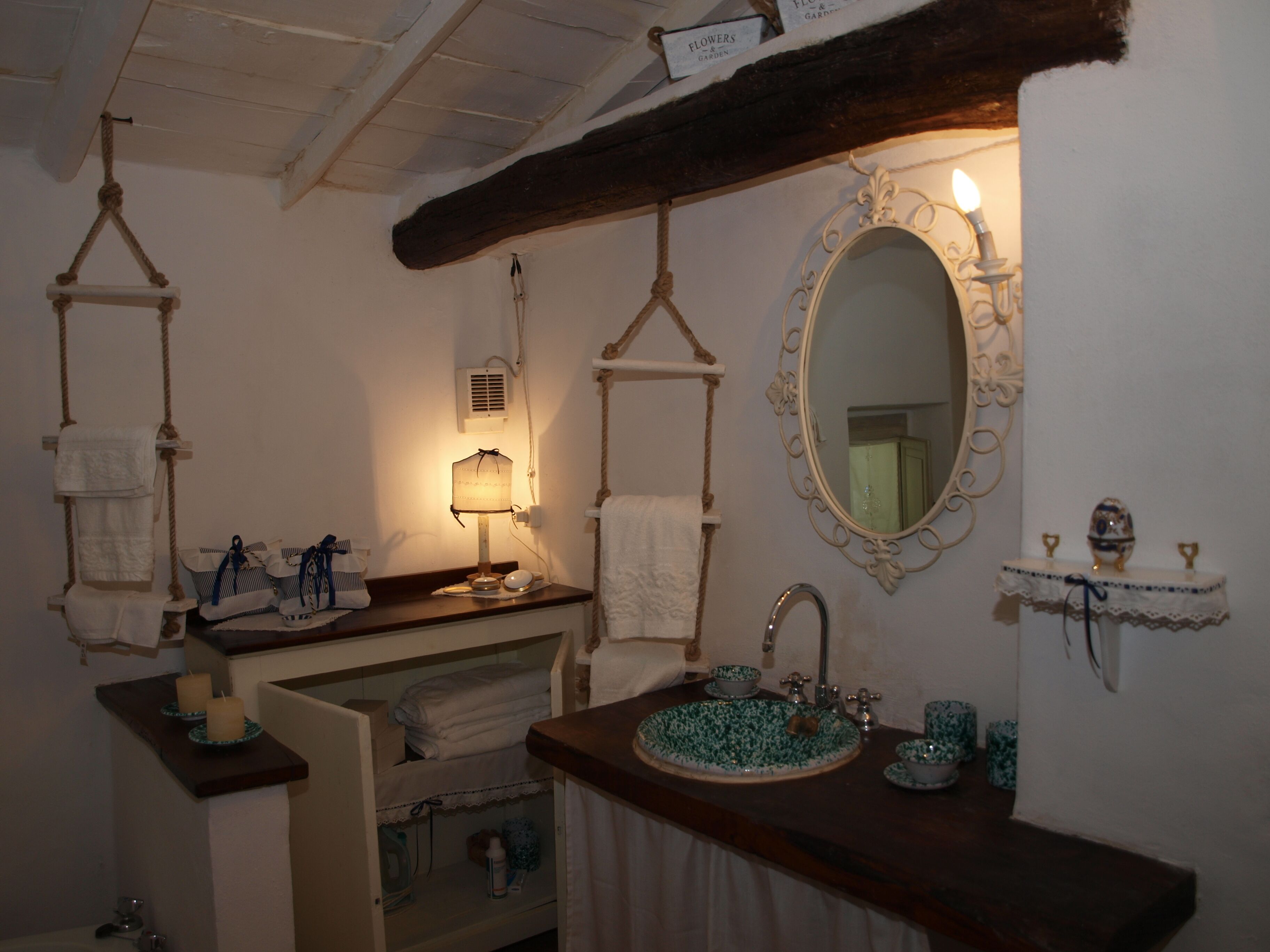 Un baño con tocador de madera, un espejo redondo con marco decorativo, un perchero para toallas y un estante con artículos de aseo.