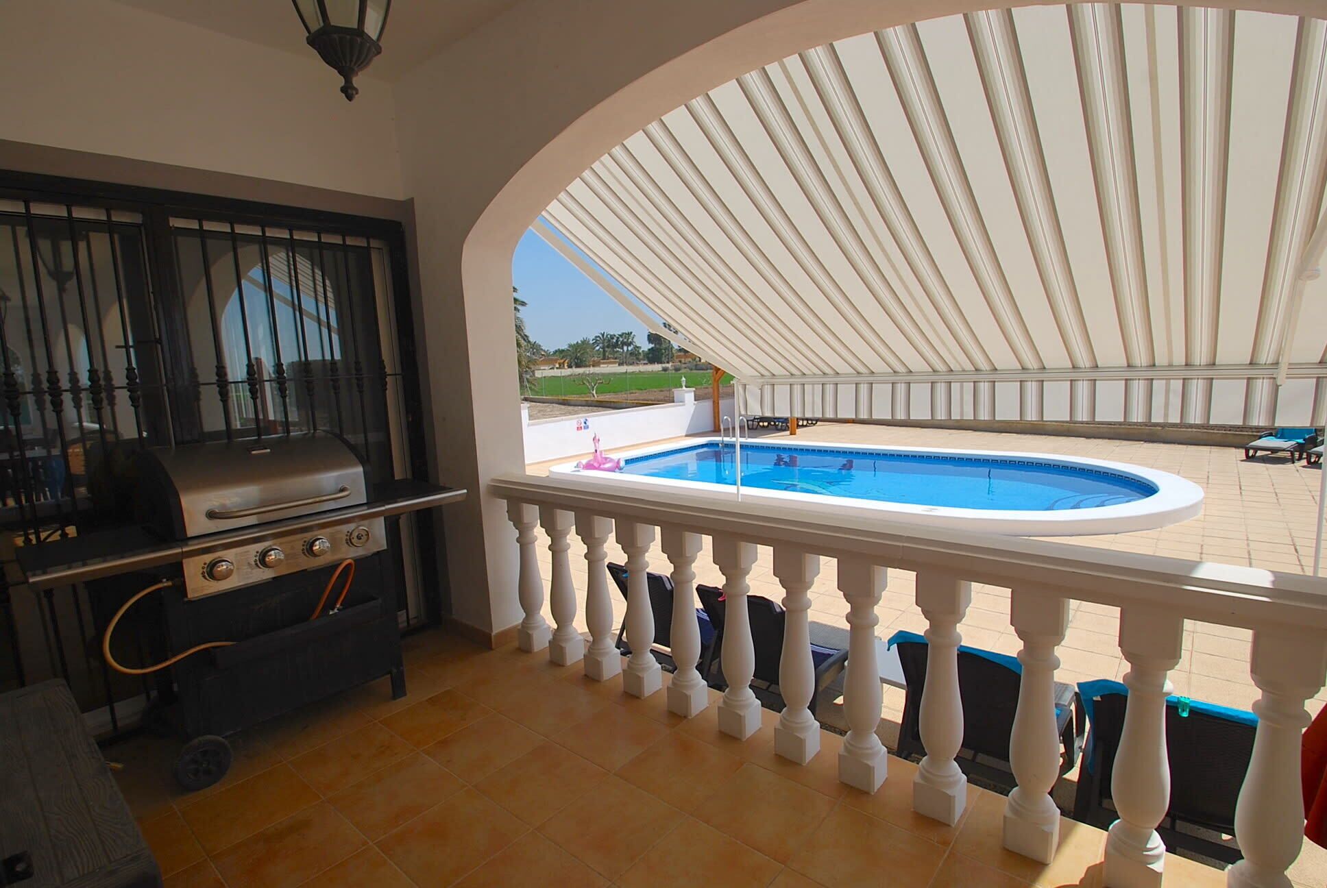 A balcony with a grill, a pool, and a view of the outdoors.