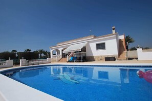 A poolside view of a white building with a covered patio, a staircase, and a clear blue sky.
