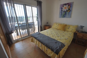 A bedroom with a bed, a nightstand, a lamp, a painting, and a sliding glass door leading to an outdoor area.