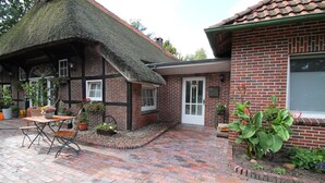Une maison traditionnelle à colombages, avec un toit de chaume et une extension en briques.