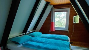 Ein kleiner, schräger Raum mit einem Bett, einem Fenster und einem kleinen Fernseher.