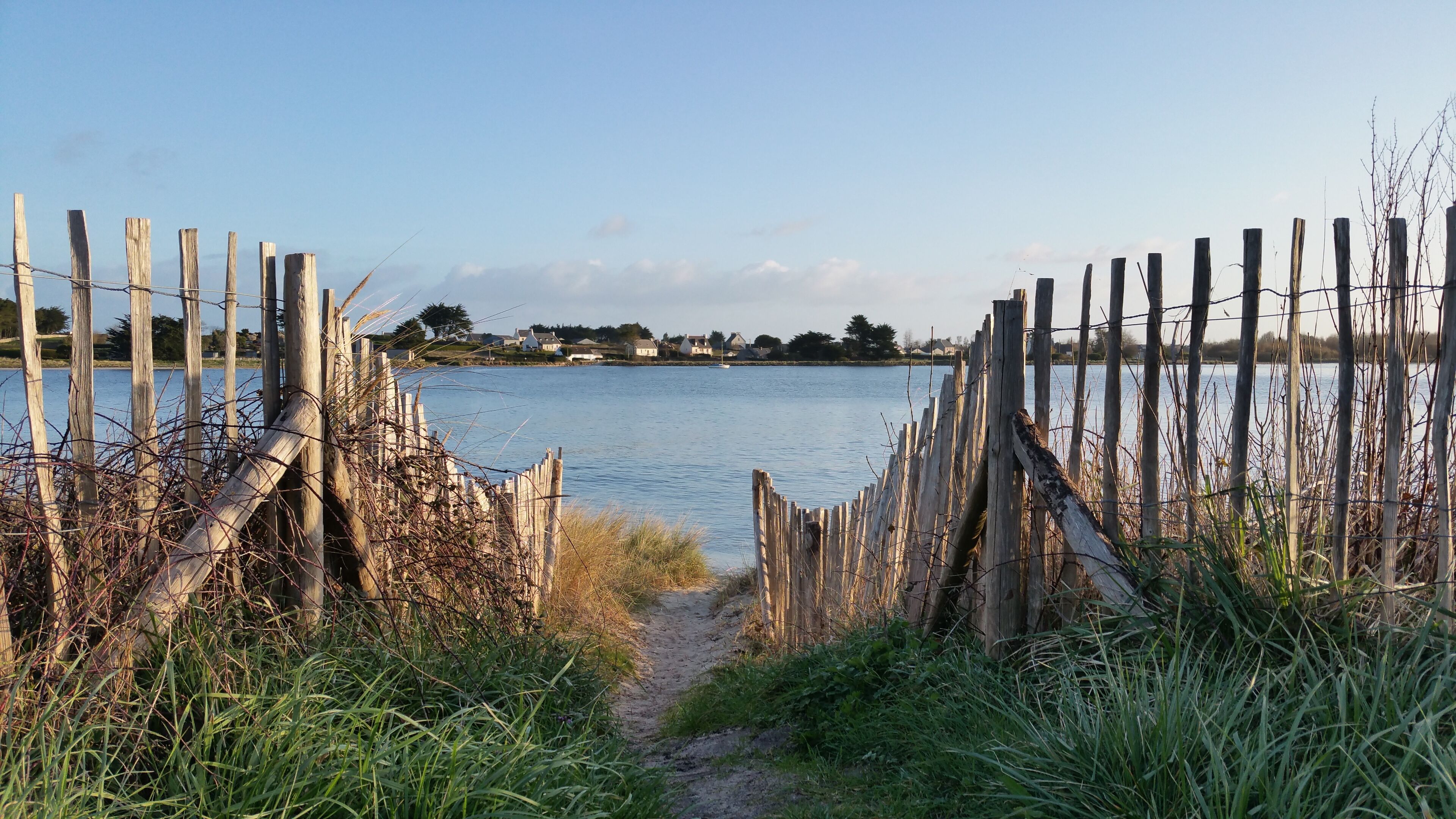 A wooden fence leading to a body of water with a path.