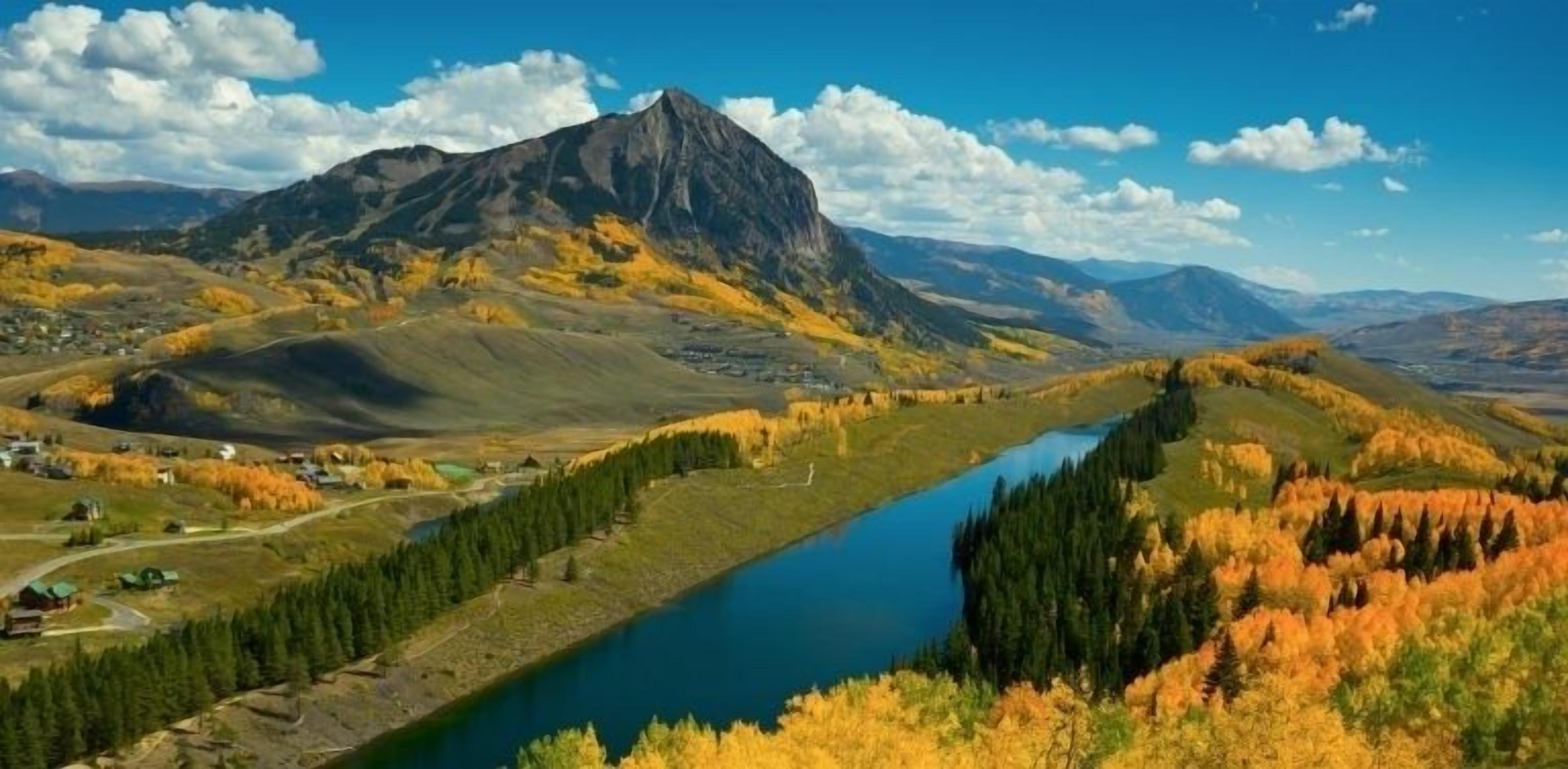 A mountainous landscape with a river, autumn foliage, and a small settlement.