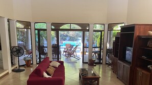 A spacious living room with a red sofa, a wooden entertainment unit, and a view of an outdoor patio area with a pool and furniture.