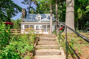 A house with a stone chimney, a wooden deck, and a staircase leading to the front door. - Classic Wisconsin Lake Home on Big Silver Lake, Great for Swimming & Boating! (Wautoma)