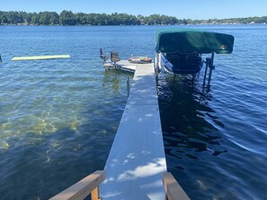 A wooden dock extending into a lake with a boat covered by a green tarp.