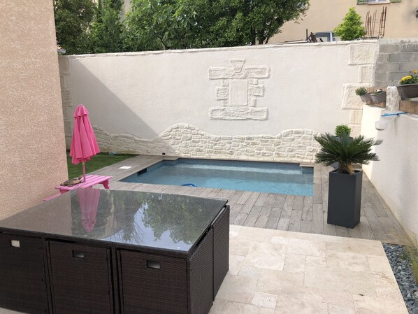 A swimming pool with stone wall design, a wooden deck, and a pink umbrella.