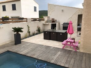 A backyard with a pool, a wooden deck, a grill, and a seating area with a pink umbrella.