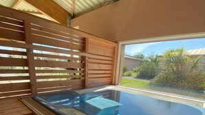 A hot tub area with wooden steps leading up to it, a window with a view of greenery, and a metal roof structure.