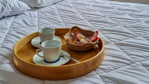 A bed with a wooden tray holding cups and pastries, a vase with flowers, and a window with a view of trees.