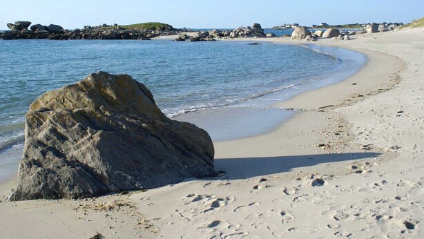 A sandy beach with large rocks and footprints.