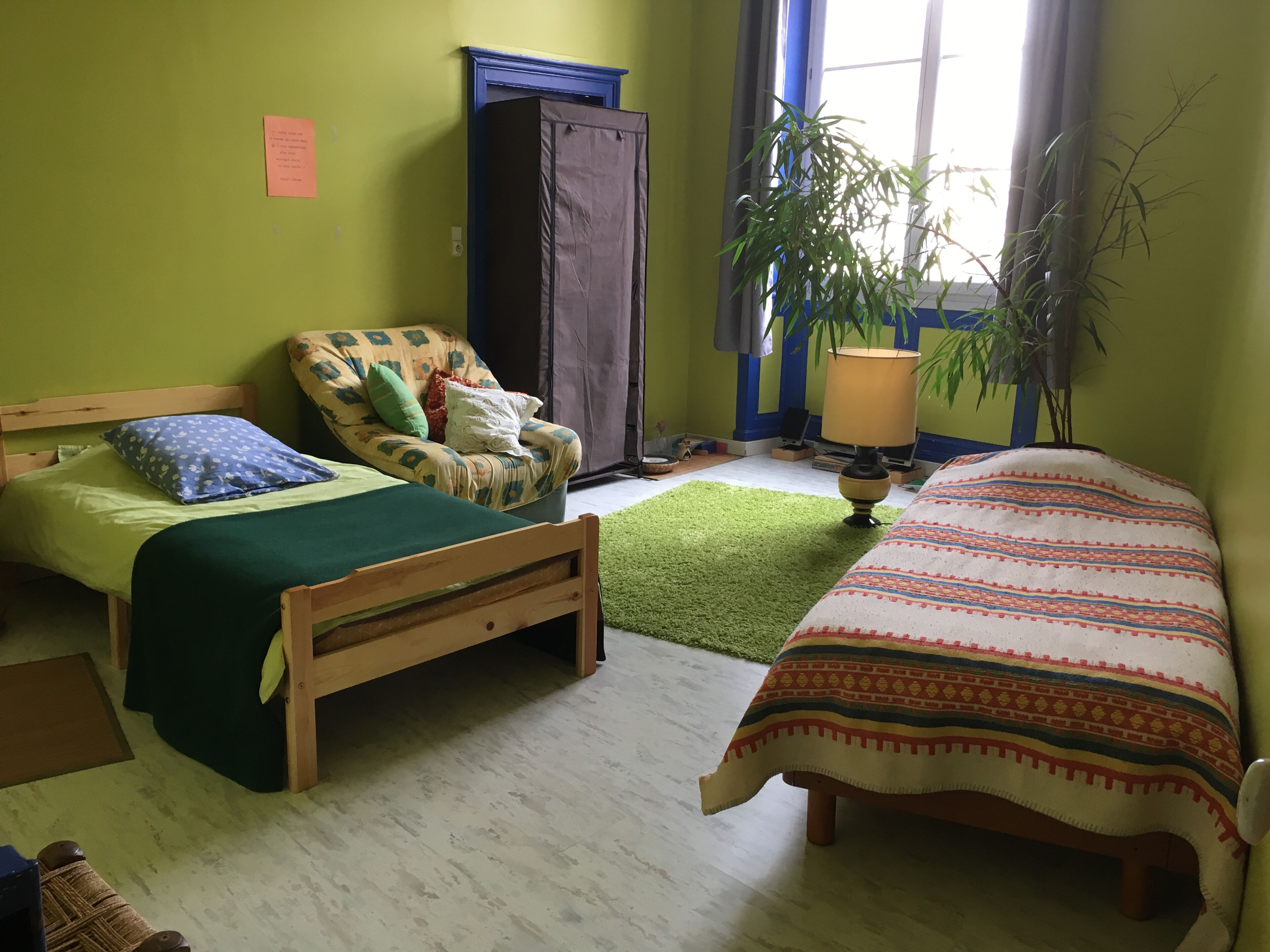 Une chambre avec deux lits, une chaise, une lampe et une fenêtre avec des rideaux.