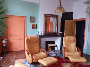 A living room with two leather armchairs, a fireplace, a mirror, and a hanging light fixture. - Large apartment downtown, quiet, comfortable, free tea, coffee (Dole)