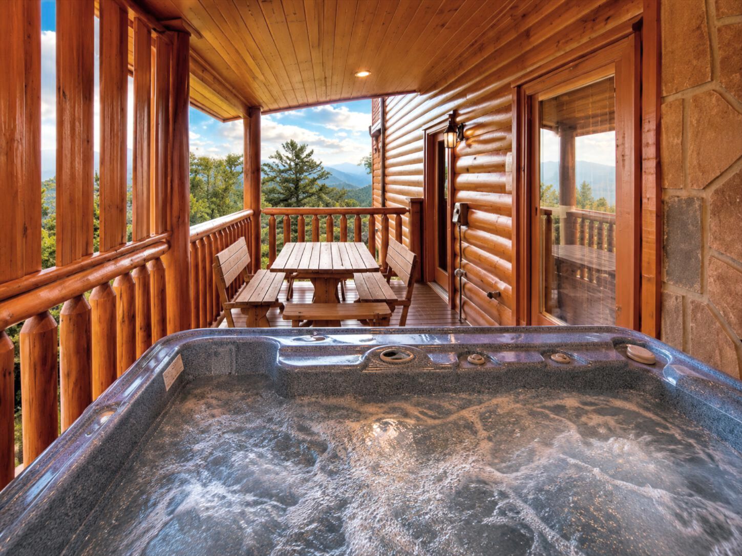 Une cabane en bois dotée d’un bain à remous, d’une terrasse en bois et d’une table avec des bancs.