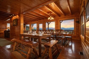 L’intérieur d’un chalet en bois comprend une table à manger pour quatre personnes, des bancs en bois et de grandes fenêtres offrant une vue sur les montagnes.