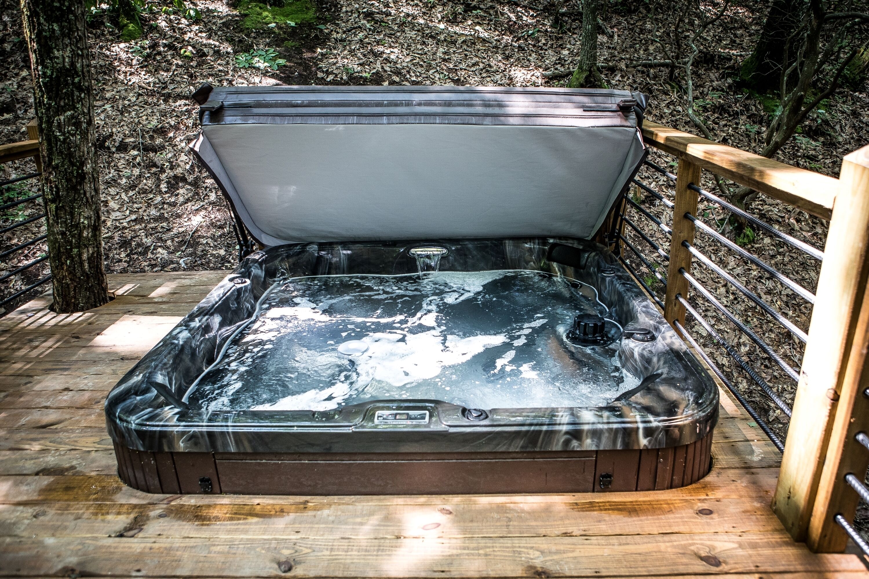 A hot tub on a wooden deck surrounded by trees.