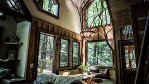 L’intérieur d’un chalet rustique, doté de grandes fenêtres, de poutres en bois et d’un coin salon accueillant.