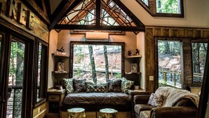 Un chalet confortable avec un grand lit, des poutres en bois et de nombreuses fenêtres offrant une vue sur la forêt.
