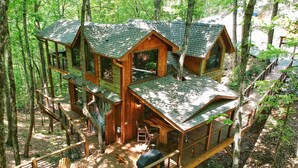 Une cabane en bois à plusieurs niveaux, dotée d’une terrasse, d’un espace salon extérieur et d’un coin barbecue, le tout entouré d’une forêt.