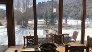 A wooden dining table with chairs and a large window overlooking a snowy outdoor area with trees and a fence. -  Gorgeous Pet-friendly Boutique Ranch ! Next to  skiing, fishing, rafting  (Snowmass)