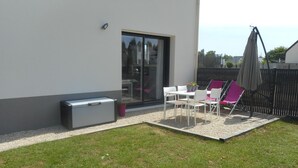 Een terras met tafel en stoelen, een klein tuinpartijtje, en een schuifdeur naar een ruimte binnen.