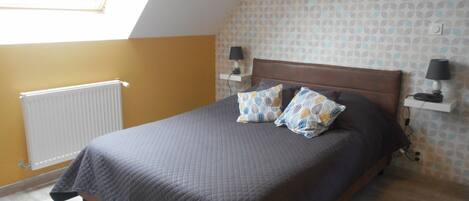 A bedroom with a sloped ceiling, a bed with a dark headboard, two bedside lamps, and patterned pillows.