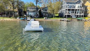 A clear waterfront view with a dock extending into the water, surrounded by residential houses. - Experience lake life at our 3-bedroom beachfront cottage, near Grand Rapids. (Rockford)