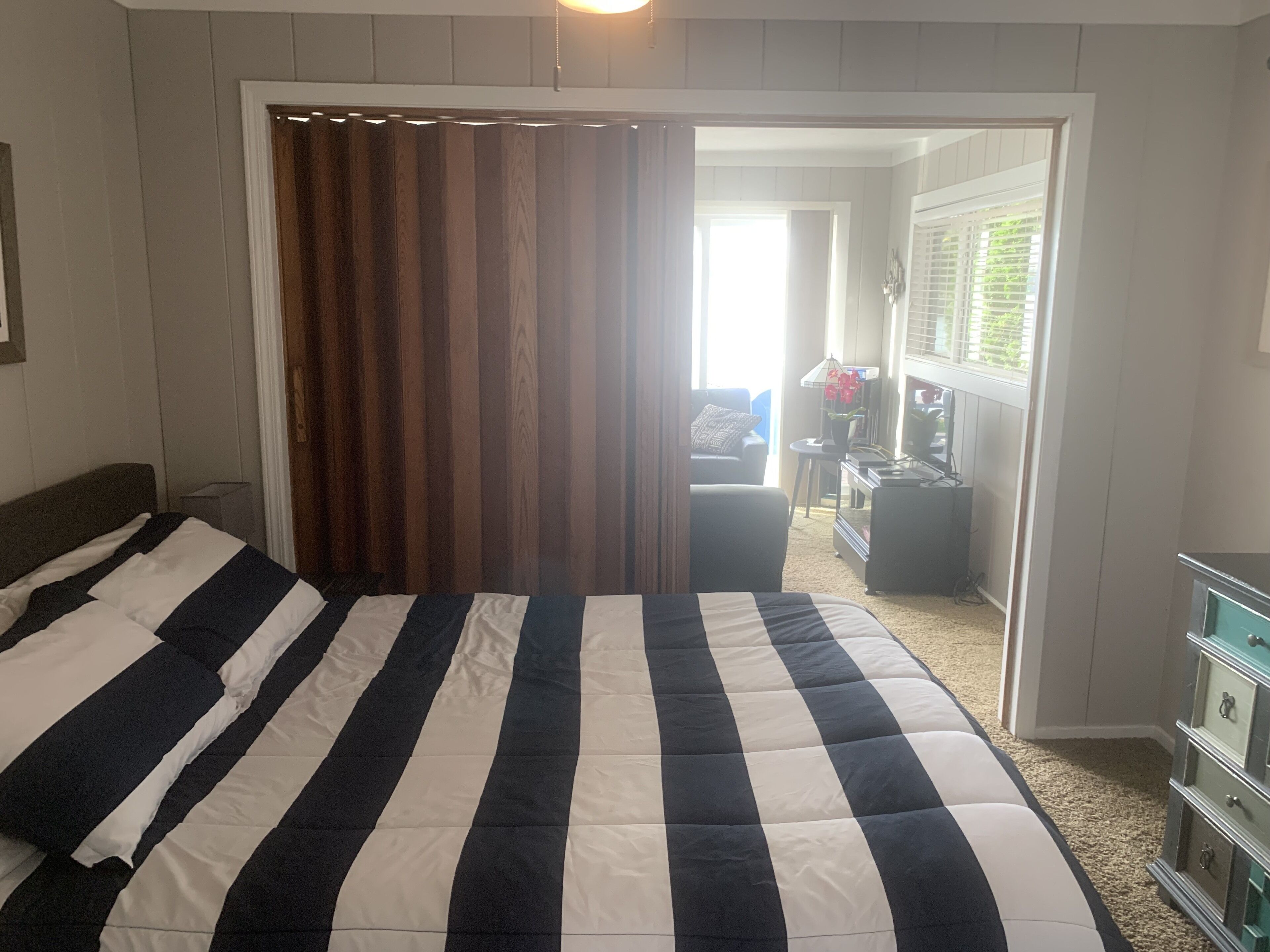 A bedroom with a large bed, a wooden door, and a view of the living area.