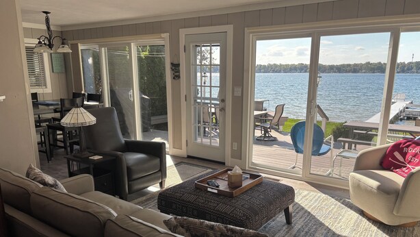A spacious living room with a large sliding glass door leading to an outdoor deck with a view of a lake. - Experience lake life at our 3-bedroom beachfront cottage, near Grand Rapids. (Rockford)