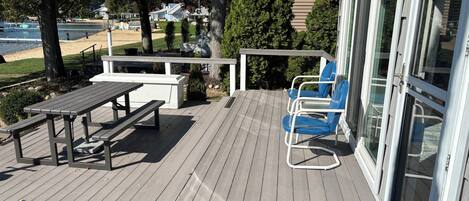 Una terraza de madera con una mesa y sillas, con vistas a un cuerpo de agua y un parque.