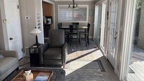 A living room with a sofa, a coffee table with a book, a lamp, and a dining area with a table and chairs. - Experience lake life at our 3-bedroom beachfront cottage, near Grand Rapids. (Rockford)