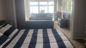 A bedroom with a large bed, a sofa, and a view of a body of water through an open door. - Experience lake life at our 3-bedroom beachfront cottage, near Grand Rapids. (Rockford)