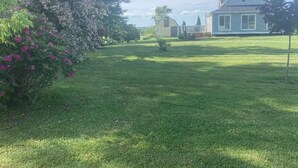 A house with a well-maintained lawn, a small garden with pink flowers, and a clear sky. - Charming 4 Bedroom Country House - 10 km from Summerside -  (Miscouche)