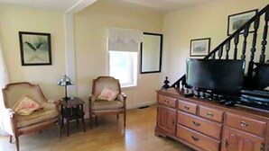 A living room with a wooden floor, a television on a cabinet, two armchairs, a small table, and a staircase. - Charming 4 Bedroom Country House - 10 km from Summerside -  (Miscouche)