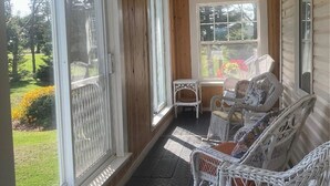 A covered porch with wicker furniture, large windows, and a view of a garden. - Charming 4 Bedroom Country House - 10 km from Summerside -  (Miscouche)