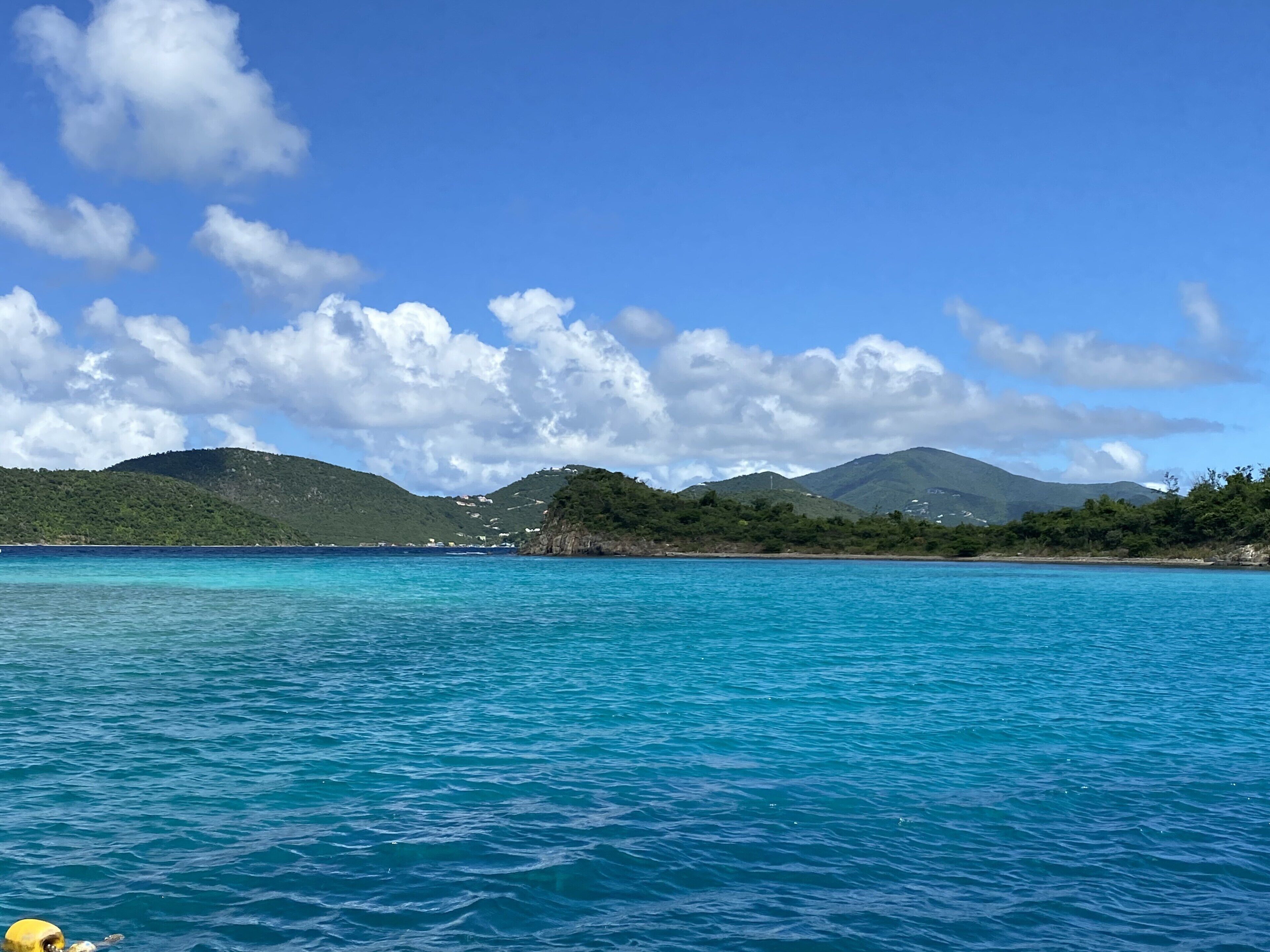 A coastal landscape with clear blue waters, green hills, and scattered buildings.