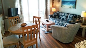A living room with a sofa, a dining table with chairs, a TV, and a painting on the wall.