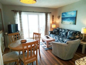 Uma sala de estar com sofá, mesa de jantar com cadeiras, televisão e um quadro na parede.