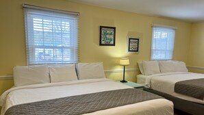 A room with two beds, white bedding, a lamp, and two framed motivational quotes on the wall.