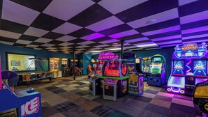 An arcade with various gaming machines, checkered floor, and a blue wall with a framed picture.