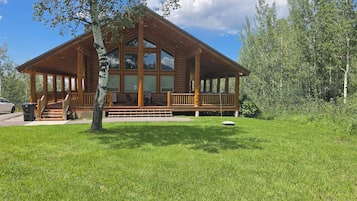 A log cabin with a porch, large windows, and a grassy yard.