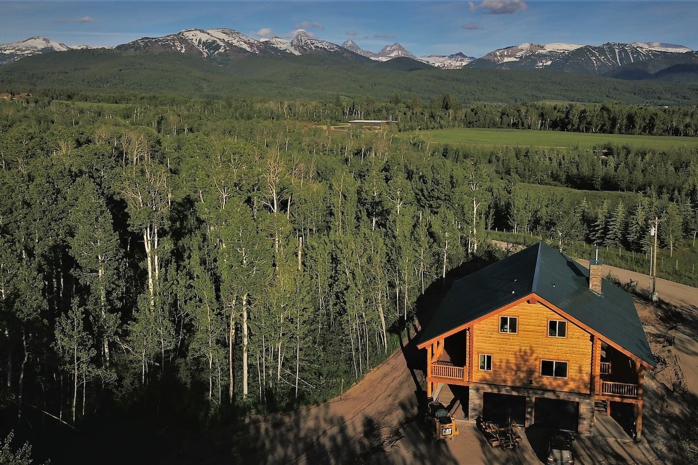 Une cabane à toit sombre, entourée d’une forêt dense, avec des montagnes en arrière-plan.