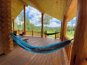 A wooden deck with a hammock, outdoor furniture, and a view of the landscape.