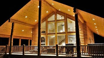 A log cabin with a large central window, a balcony, and a staircase leading to an upper level.
